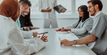 A group of multiethnic medical professionals including doctors, surgeons, and nurses are gathered in a hospital setting discussing patient care and using modern technology to address challenges in the medical field. A group of multiethnic medical professionals including doctors, surgeons, and nurses are gathered in a hospital setting discussing patient care and using modern technology to address challenges in the medical field